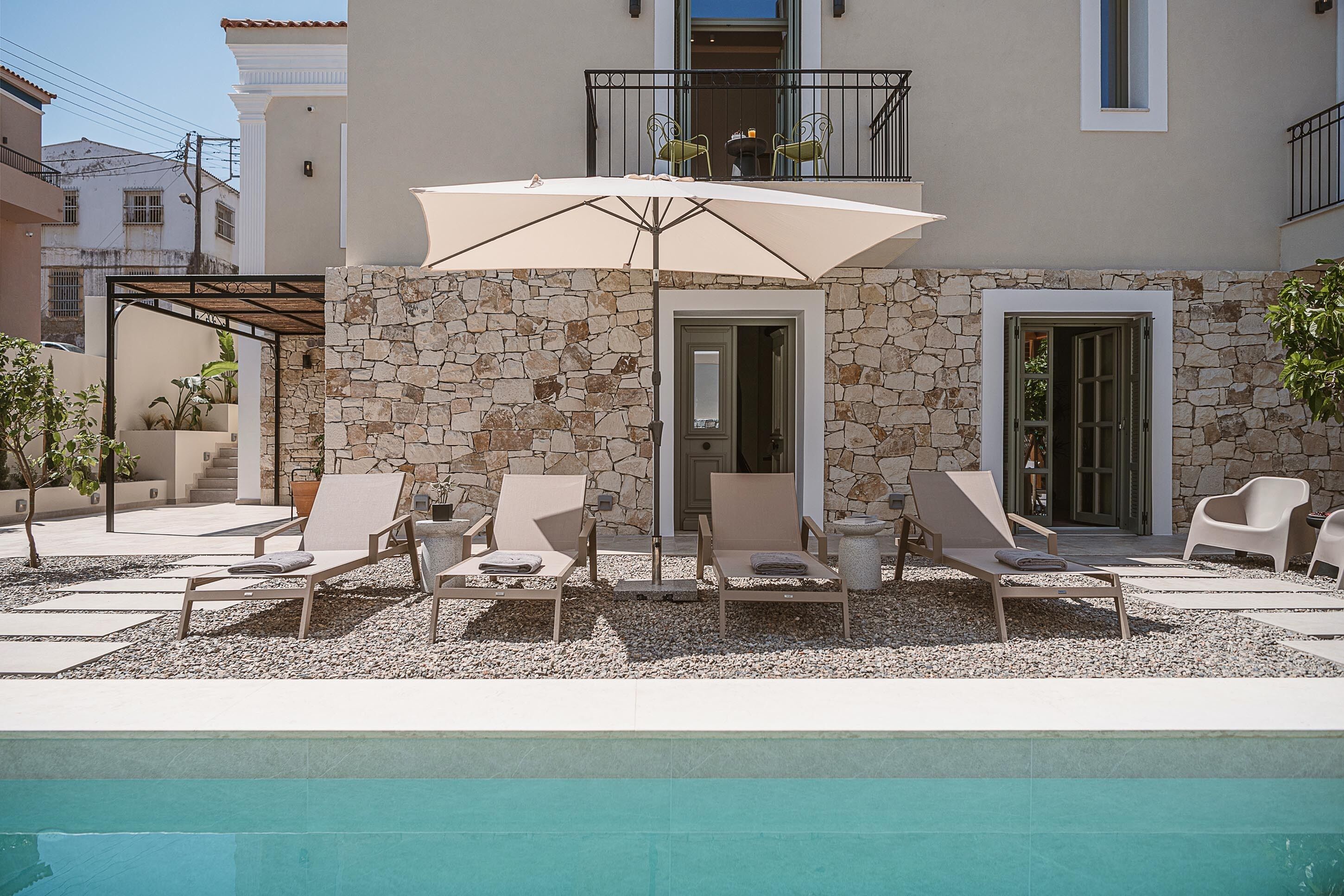 Un espace aménagé au bord de la piscine, avec des chaises longues, un grand parasol et un mur en pierre.