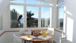Ein Essbereich mit Tisch, gedeckt für das Frühstück, große Fenster mit Blick auf das Meer und ein heller, weißer Innenraum.