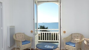 Ein Balkon mit zwei Korbstühlen und einem kleinen Tisch, mit Blick auf ein Gewässer und eine entfernte Landmasse.
