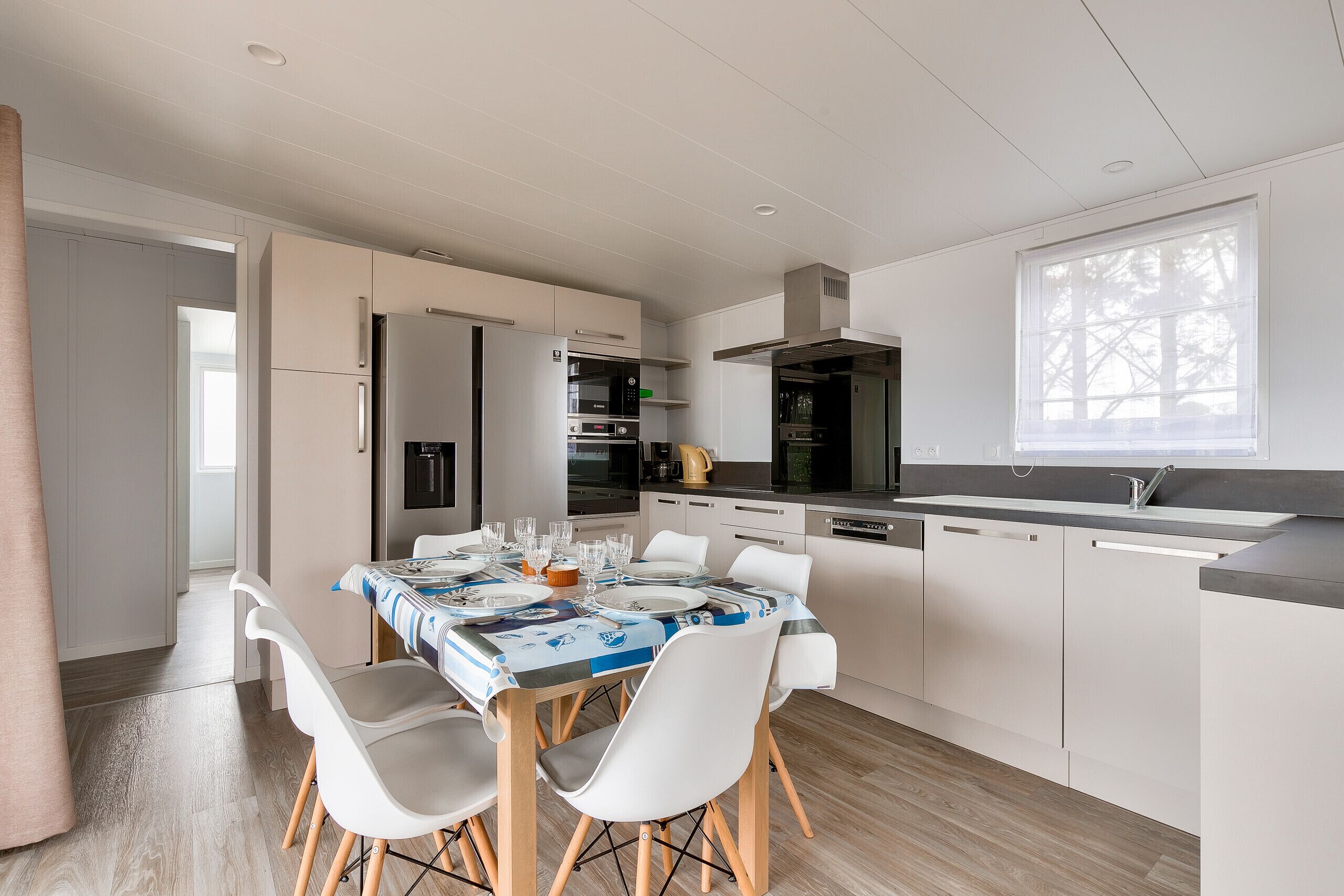 A modern kitchen with white cabinetry, a dining table set for four, and a large window providing natural light.