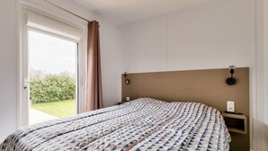 Un dormitorio con cama, mesita de noche y cortinas en la ventana, con vista a espacios verdes.