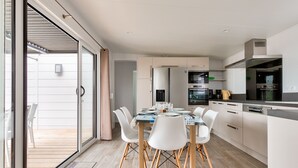 Una cocina moderna con armarios blancos, un comedor con sillas blancas y un amplio ventanal corredero que da a un espacio exterior.