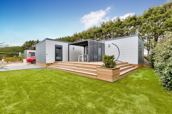 A modern, two-story house with a covered patio, a small garden, and a red car parked outside.