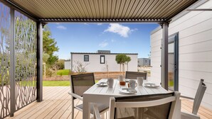 Un patio al aire libre con una mesa y sillas, una pérgola arriba y una vista de un edificio moderno al fondo.