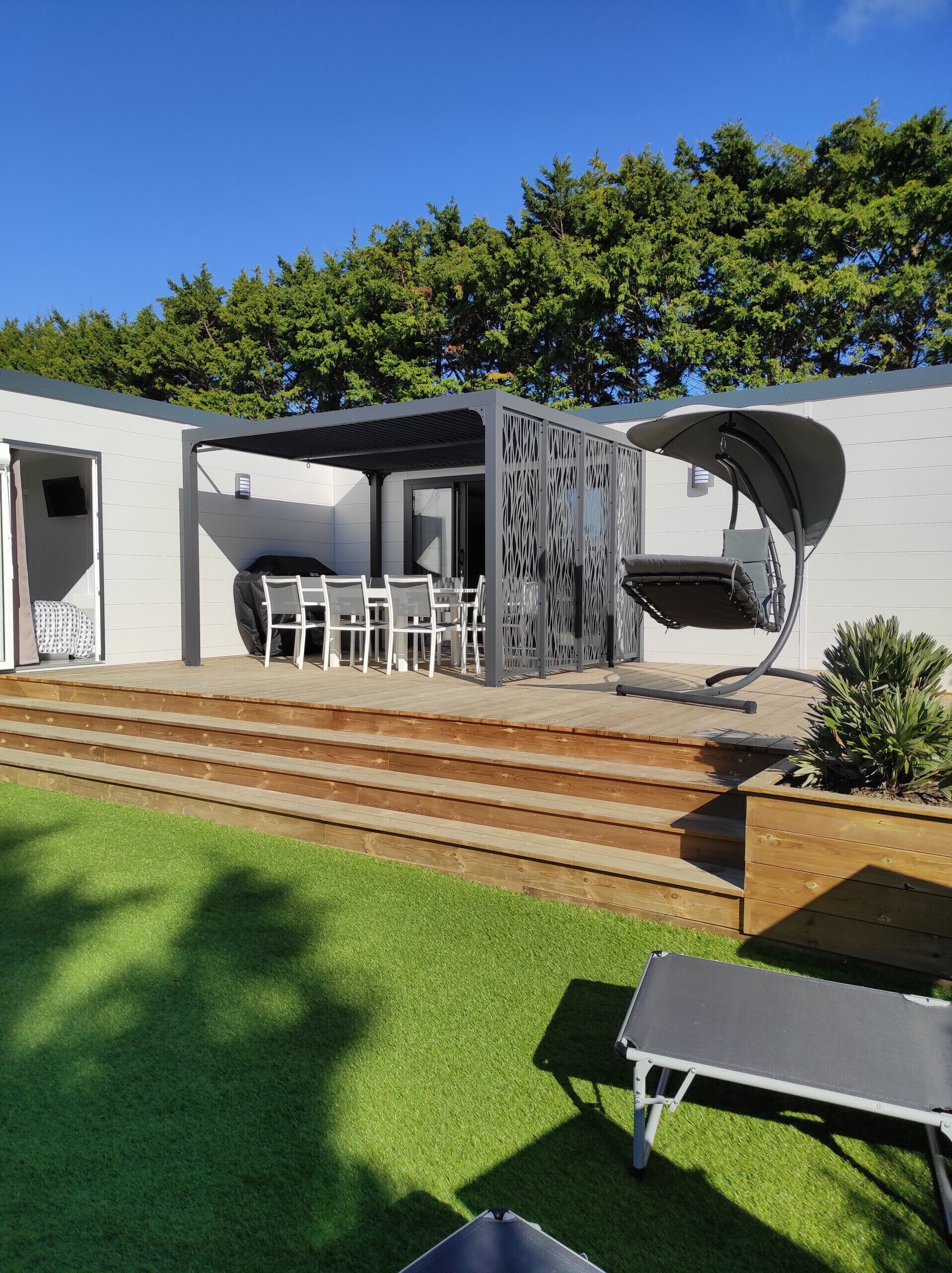 Un patio con una parrilla, mobiliario exterior y una estructura de pérgola.