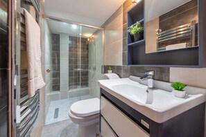 A modern bathroom with a glass shower enclosure, a white toilet, a large sink with a mirror above it, and two potted plants.