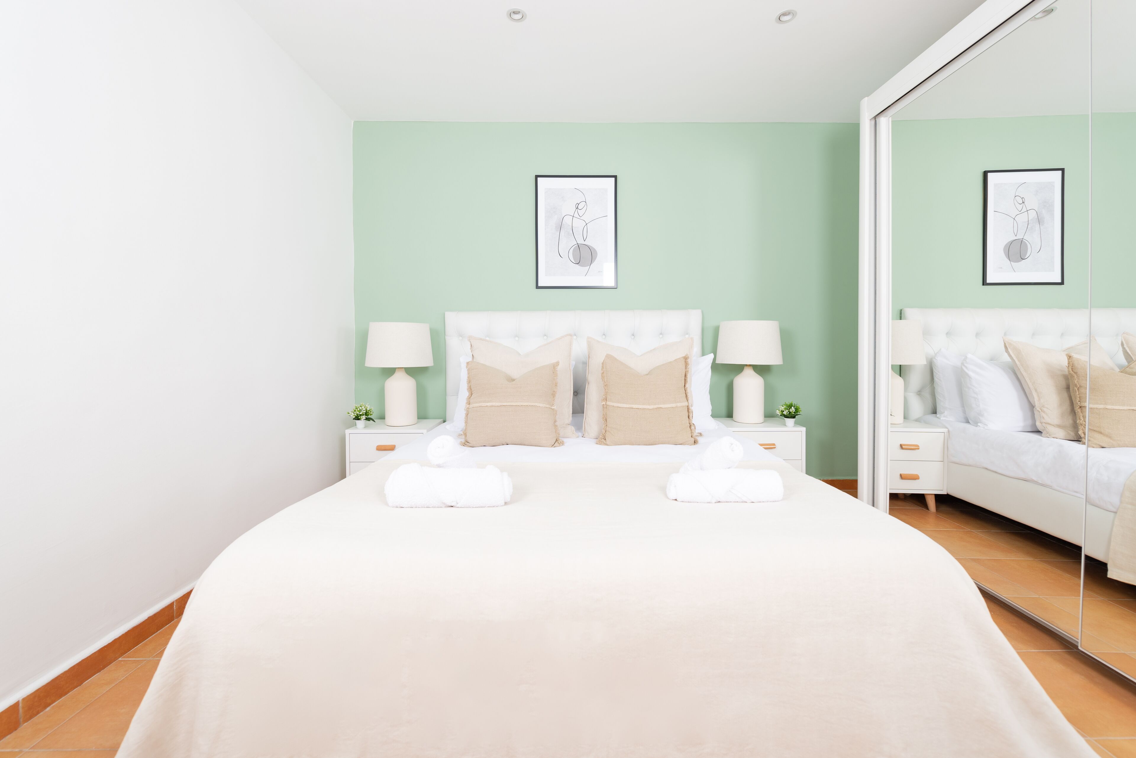 A neatly arranged bedroom with a large bed, two bedside tables with lamps, and a mirror on one wall.