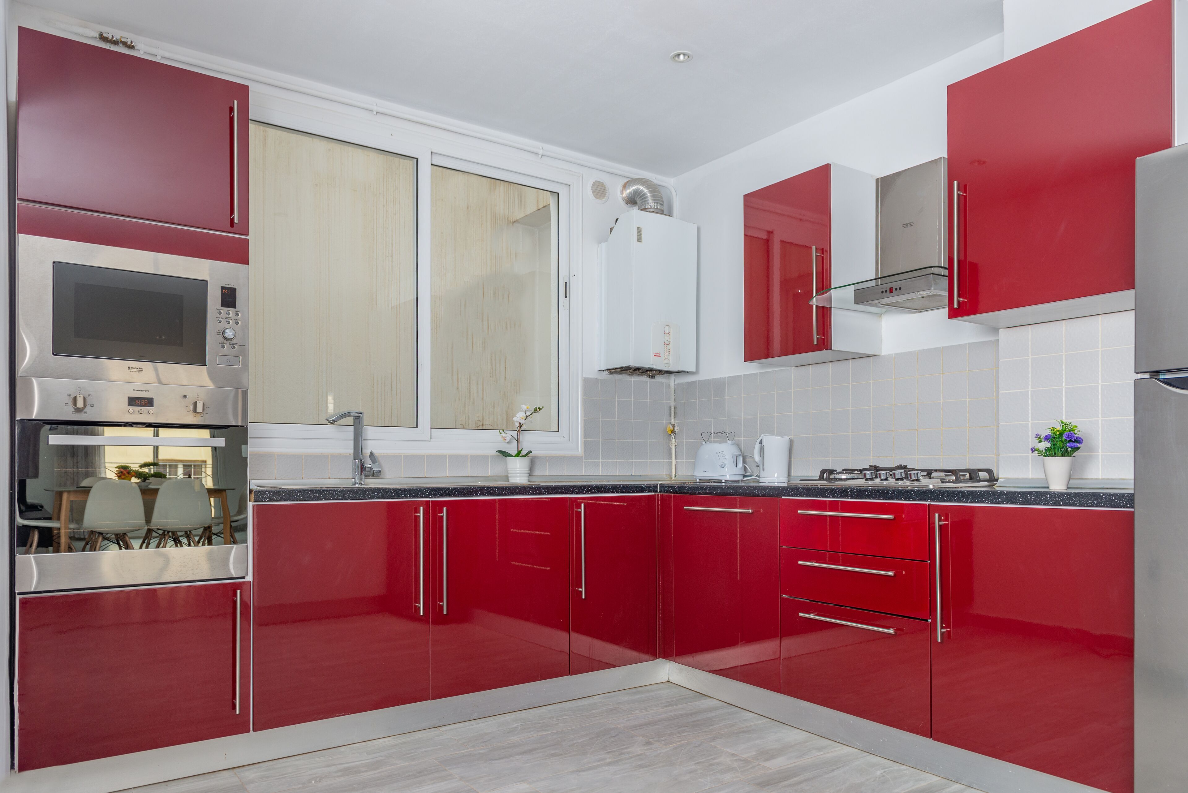Una cucina moderna con mobili rossi, elettrodomestici in acciaio inossidabile e una parete di fondo rivestita di piastrelle.