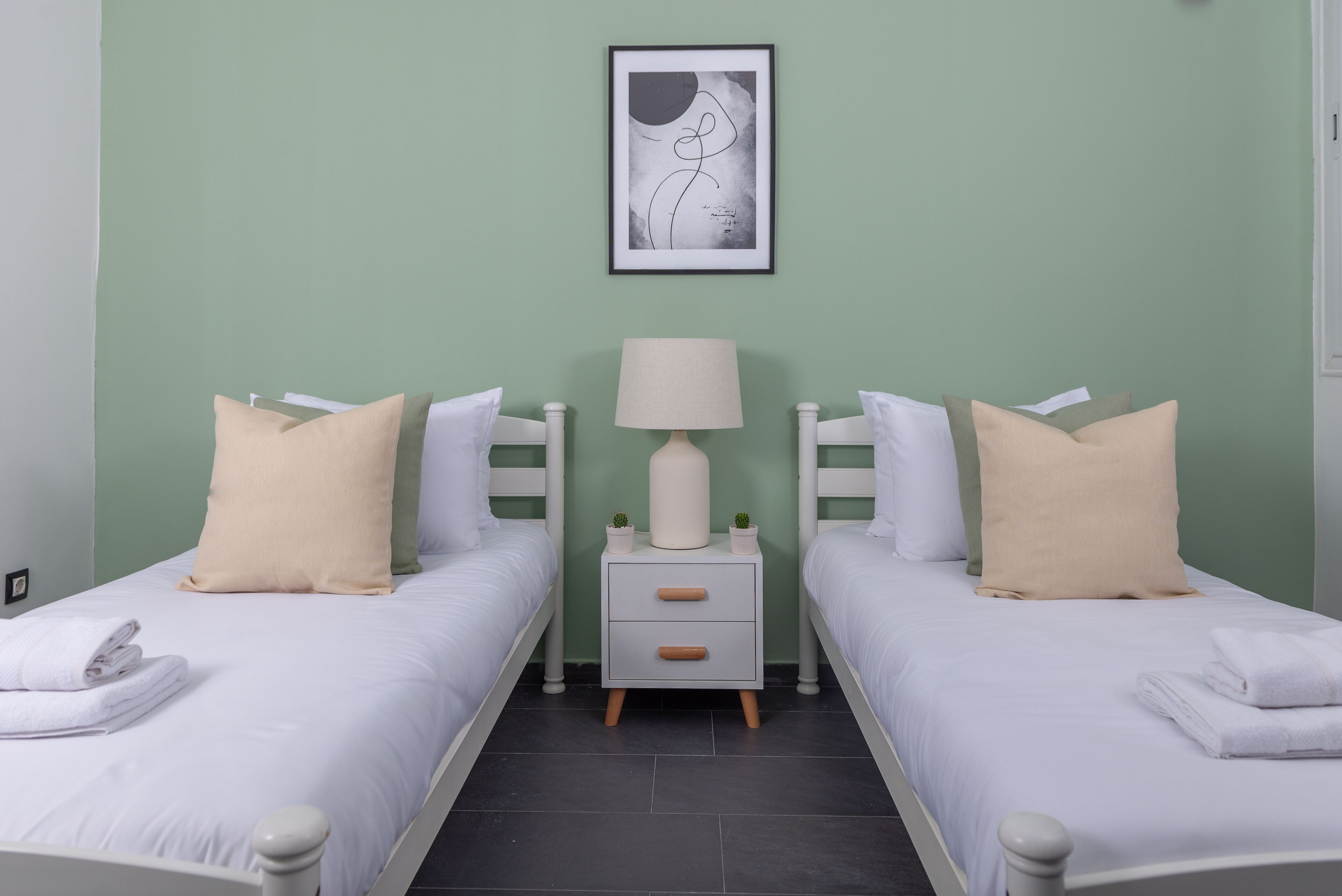 Habitación doble con dos camas, una mesita de noche con lámpara y una obra enmarcada en la pared.