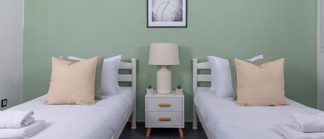 Habitación doble con dos camas, una mesita de noche con lámpara y una obra enmarcada en la pared.