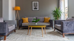 Ein modernes Wohnzimmer mit einem grauen Sofa, gelben Kissen, einem runden Couchtisch und einer Stehlampe.