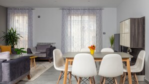 Ein modernes Wohnzimmer mit einem grauen Sofa, einem Esstisch mit weißen Stühlen und einer grauen Kommode.