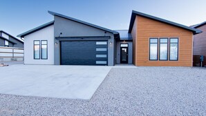 A modern two-story house with a garage, a driveway, and a gravel area. - Desert Dreams Moab with Home EV Charging (Moab)