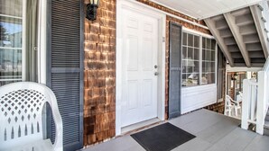 A house entrance with a white door, a porch with a white chair, and a small outdoor seating area.