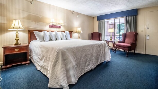 Una habitació d'hotel amb un llit gran, dues làmpades de nit, una cadira, una taula petita i una finestra amb cortines.
