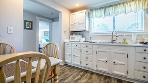 A compact kitchen with white cabinets, a microwave, and a sink. There is a dining area with a wooden table and chairs. - Jacuzzi room - 2 Queen beds (OGUNQUIT)