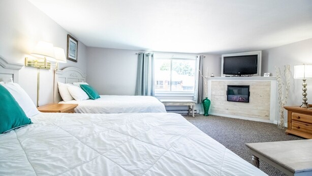 A hotel room with two beds, a television, a fireplace, and a window with curtains. - Jacuzzi room - 2 Queen beds (OGUNQUIT)