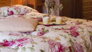 Een slaapkamer met een bloemenbedekker, een nachtkastje met een lamp en een kaptafel met een spiegel.