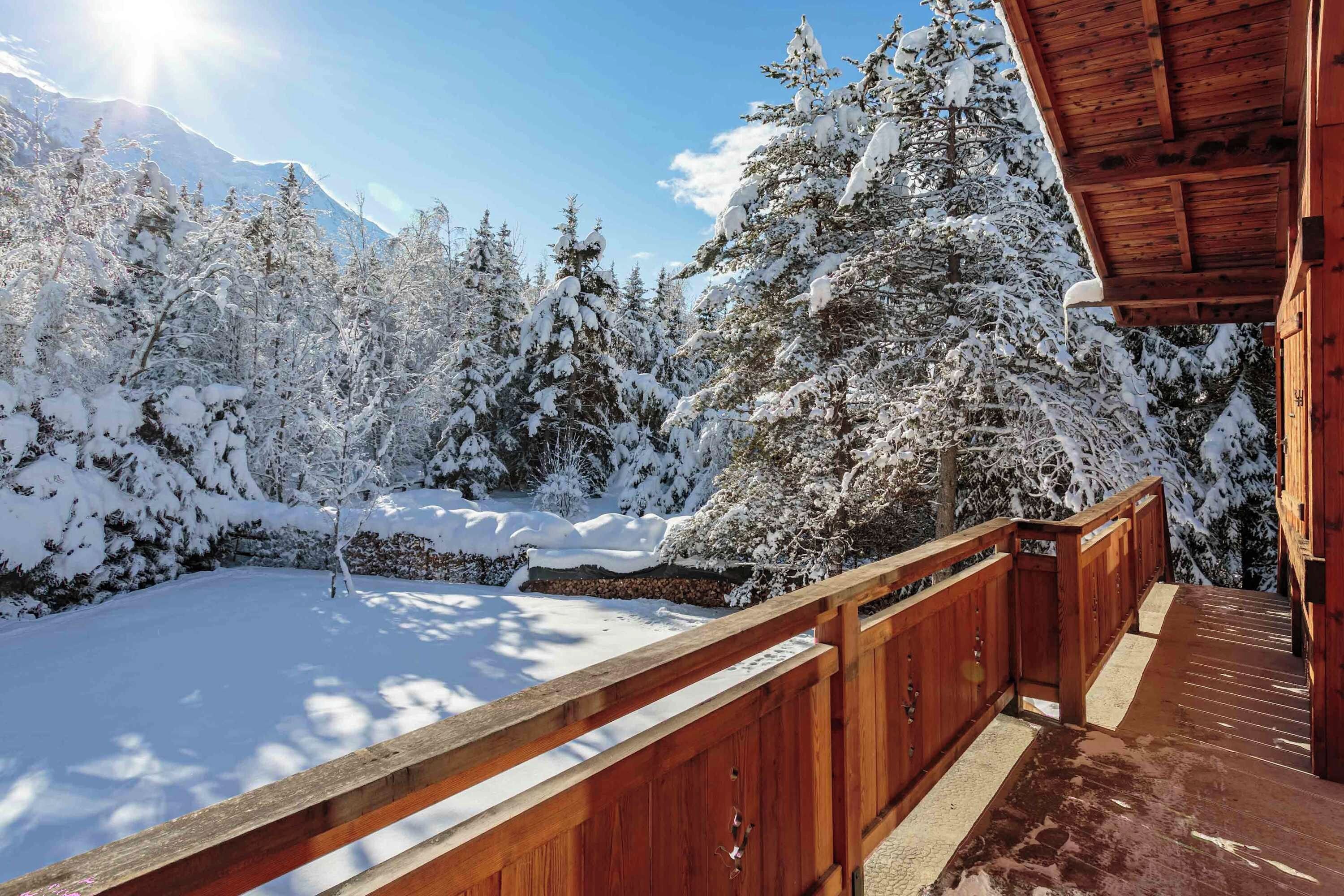 A wooden deck with a view of snow-covered trees and a mountain in the background.