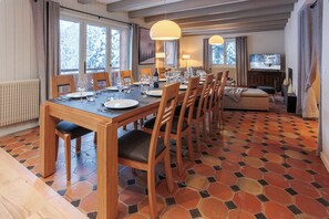 Un coin repas avec une table en bois dressée pour six personnes, entourée de chaises, et offrant une vue sur les arbres enneigés à travers de grandes fenêtres.