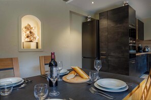 Une cuisine moderne aux meubles sombres, une table à manger dressée avec des assiettes, des verres et des couverts, et une bouteille de vin.