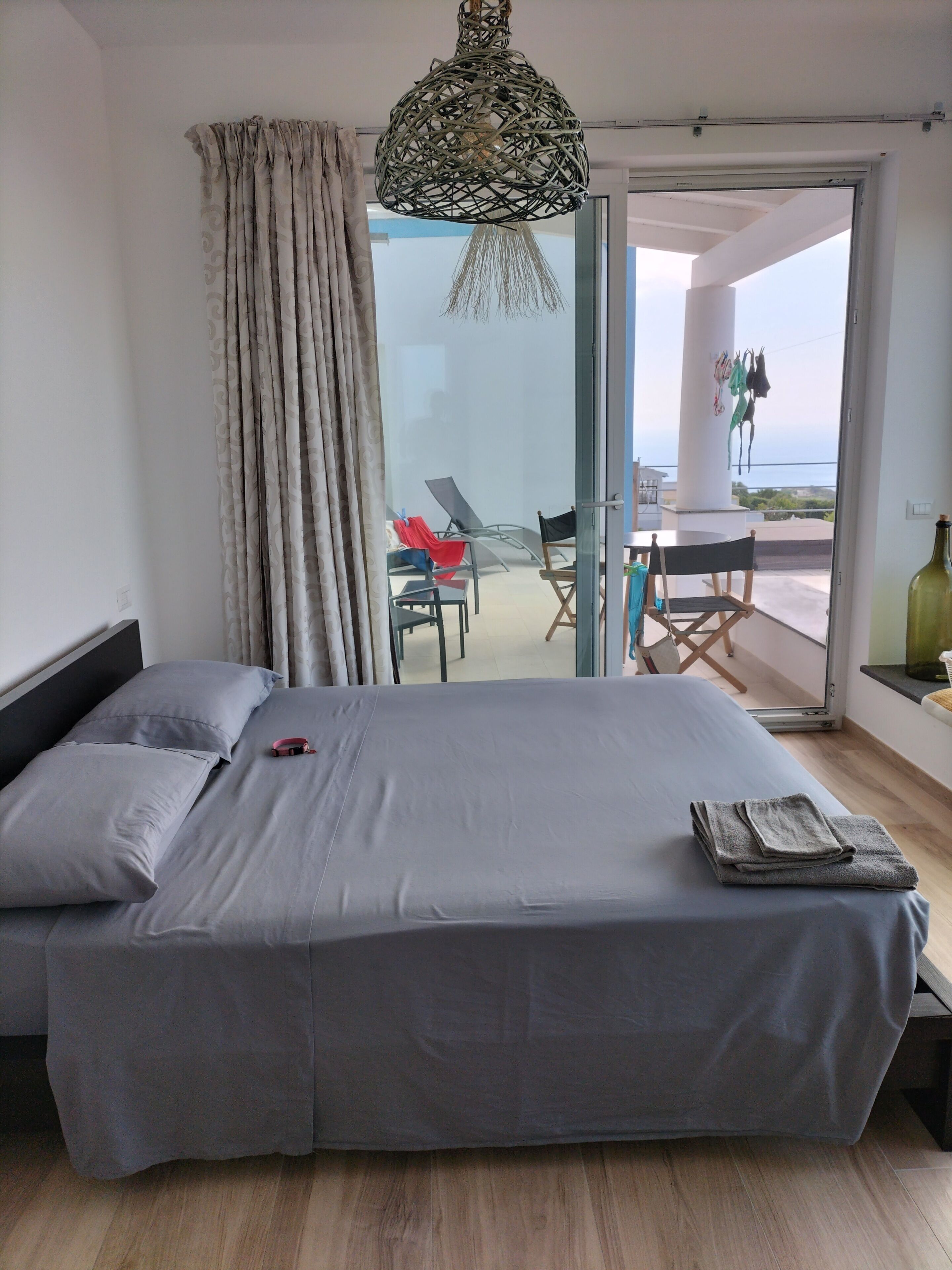 Un dormitorio con una cama grande, vistas a la terraza y una lámpara colgante.