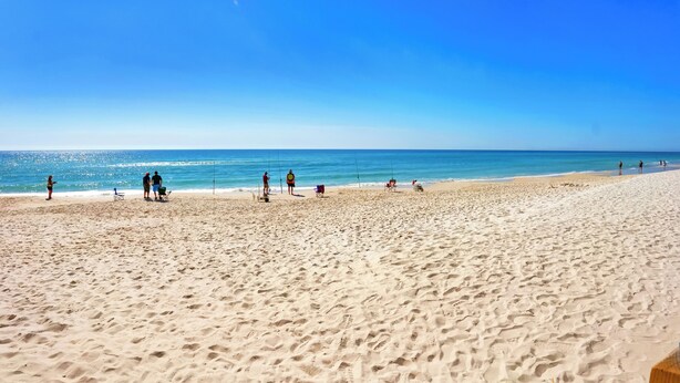 Ein weiter Sandstrand mit blauem Himmel und ruhiger See.