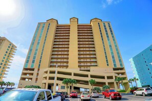 A multi-story hotel with a central atrium, parking garage, and palm trees. - Crystal Shores West 507 by Liquid Life (Gulf Shores)