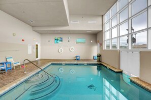 An indoor swimming pool with clear water, a lifeguard chair, and a view of palm trees through large windows. - Crystal Shores West 507 by Liquid Life (Gulf Shores)