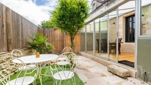 Une terrasse avec une table ronde et des chaises, une clôture en bois et un arbre.