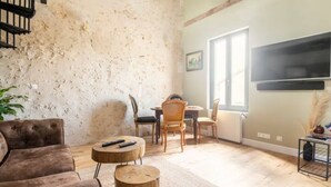 Un salon avec un mur en pierre rustique, un canapé marron, une table basse ronde et un téléviseur fixé au mur.