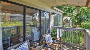A covered outdoor area with a wooden deck, wicker furniture, and a view of a lush garden. - 92 Forest Gardens: Newly Remodeled Villa, Walk to Beach, Pool, Free Bikes (Hilton Head Island)