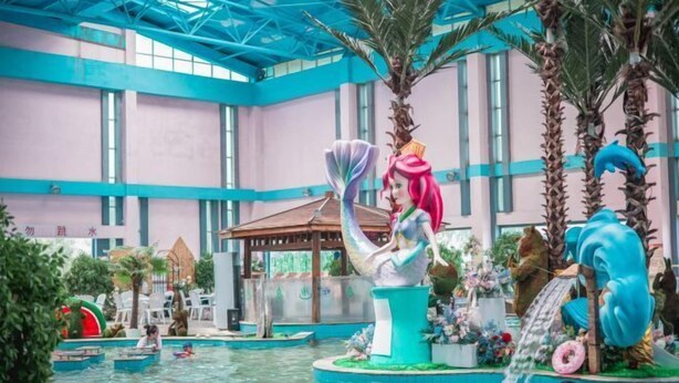 Una piscina interna con una grande statua di una sirena, palme e una cascata.