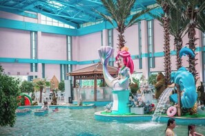 An indoor swimming pool with a large mermaid statue, palm trees, and a waterfall feature.