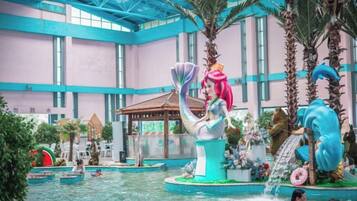 Un parque acuático interior grande con una estatua de sirena, palmeras y una cascada.