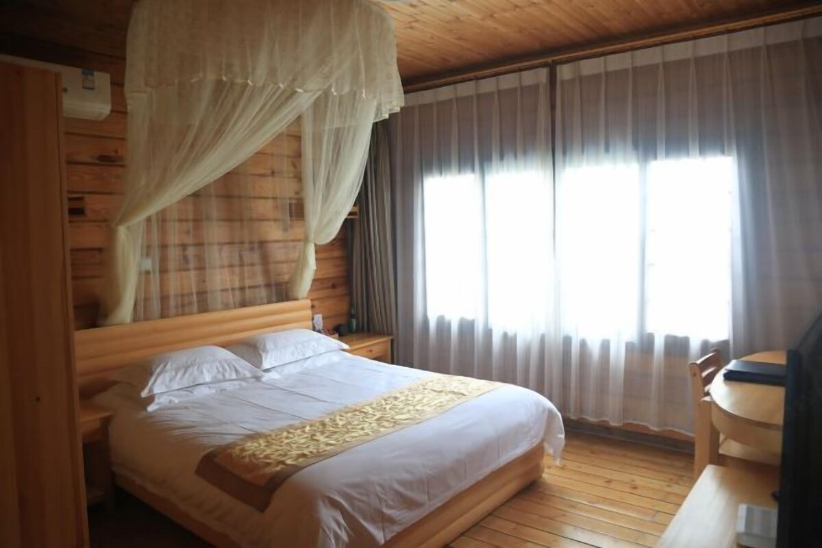 A wooden-paneled room with a bed, a nightstand, a table, and a window with curtains.