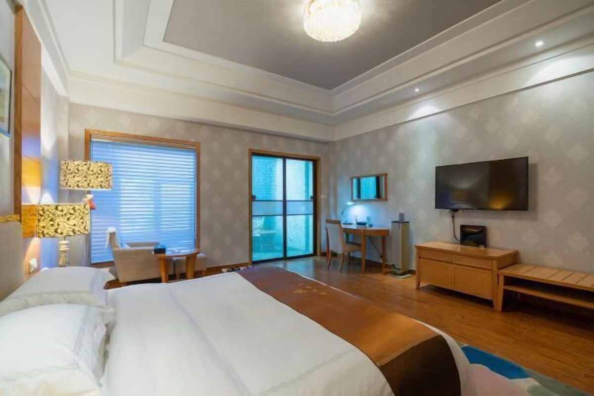 A hotel room with a large bed, a desk, a television, and a sliding door to a balcony.