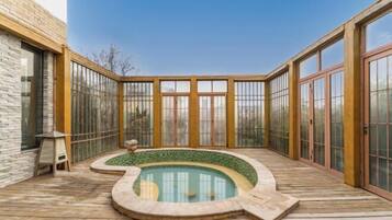 A pool area with a curved design, surrounded by glass doors and a wooden deck.