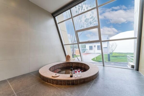 A modern spa area with a circular hot tub, a bottle of wine, and two wine glasses. - Shanghe Hotspring Hotel (Shanghe)