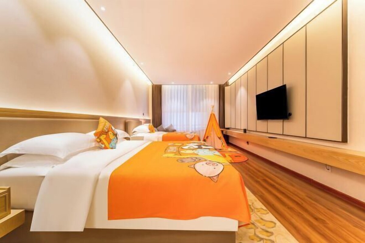 A hotel room with a bed, a flat-screen TV mounted on the wall, and a window with curtains.