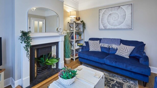 Een woonkamer met een open haard, een blauwe bank, een boekenkast en een groot abstract schilderij aan de muur.