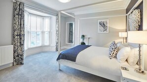 Een slaapkamer met een groot bed, een nachtkastje, een lamp en een raam met gordijnen.