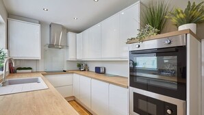 Een moderne keuken met witte kasten, een houten aanrechtblad, een ingebouwde oven en een roestvrijstalen afzuigkap.