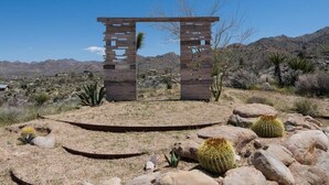 A wooden archway in a desert landscape with cacti and sparse vegetation.