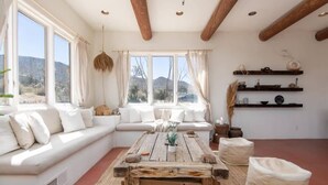 A cozy living room with a white sofa, a rustic wooden coffee table, and a view of the mountains through large windows.