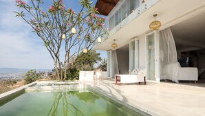 A modern outdoor pool area with a clear view of the cityscape, a large tree with pink flowers, and a white outdoor seating area. - Suite with pool and mountain view / Suite with pool and mountain view (San Andrés Huayápam)