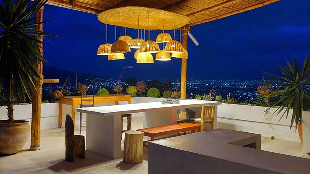 An outdoor patio with a thatched roof, hanging wicker lamps, and a view of the city at night. - Suite with pool and mountain view / Suite with pool and mountain view (San Andrés Huayápam)