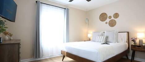 Un dormitorio con cama, ventilador de techo, televisor, ventana con cortinas y una pared decorada con platos.