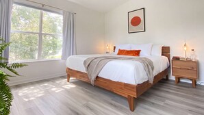 A bedroom with a bed, bedside tables, a ceiling fan, a window with curtains, and a wall-mounted artwork. - Sanctuary at Oaks | Full Kitchen • Near I75 (Gainesville)