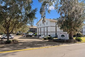 A condominium complex named "The Oaks" with a white building, parked cars, and mature trees.